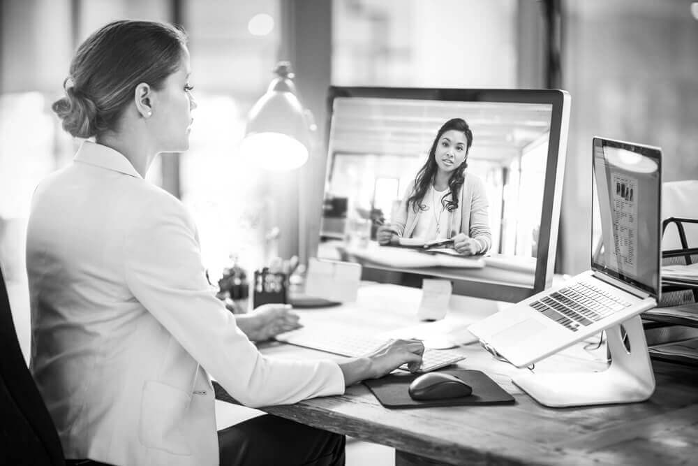 This is a photo of a woman speaking to another woman through a computer monitor.